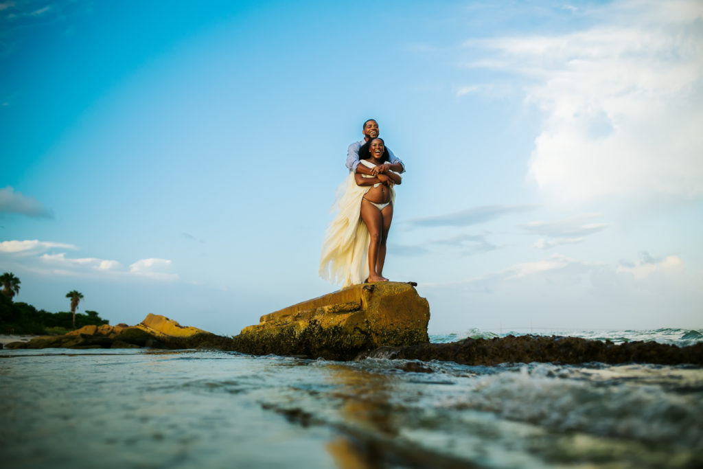 fun couples maternity photos taken of a couple standing on a rock at the beach at fort desoto 