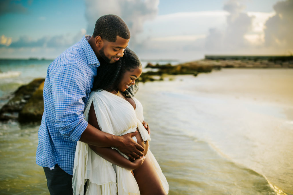 couples pregnancy session at the beach at sunset time with rocks and waves at a st Pete fl beach