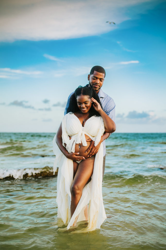 sexy couples pregnancy portraits taken in the water at the beach with a women in a boho chiffon gown with her baby bump out 
