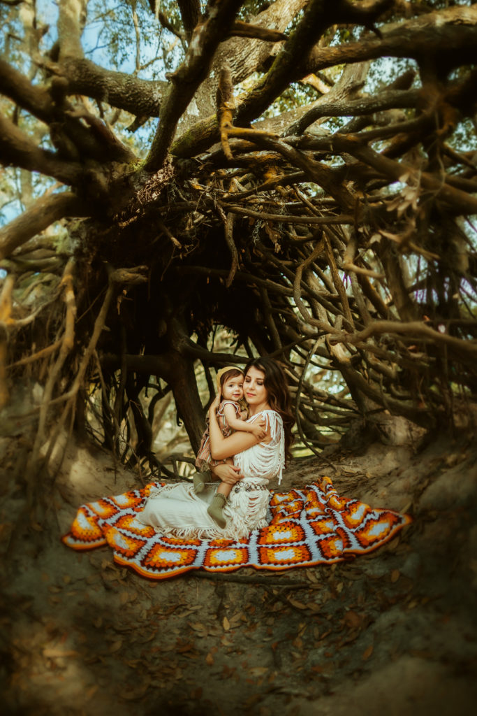 portrait of a mother and daughter hugging underneath a cool tree with exposed roots during a breastfeeding photo session