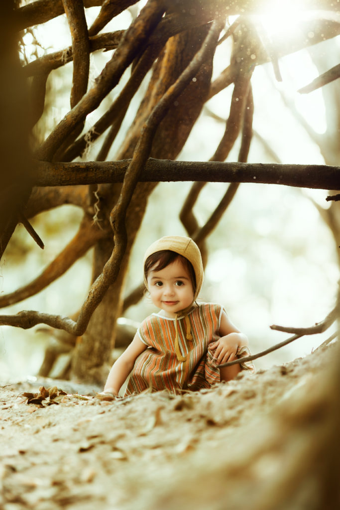 vintage styled outdoor baby photo session with a toddler in a vintage dress and bonnet playing in the dirt 