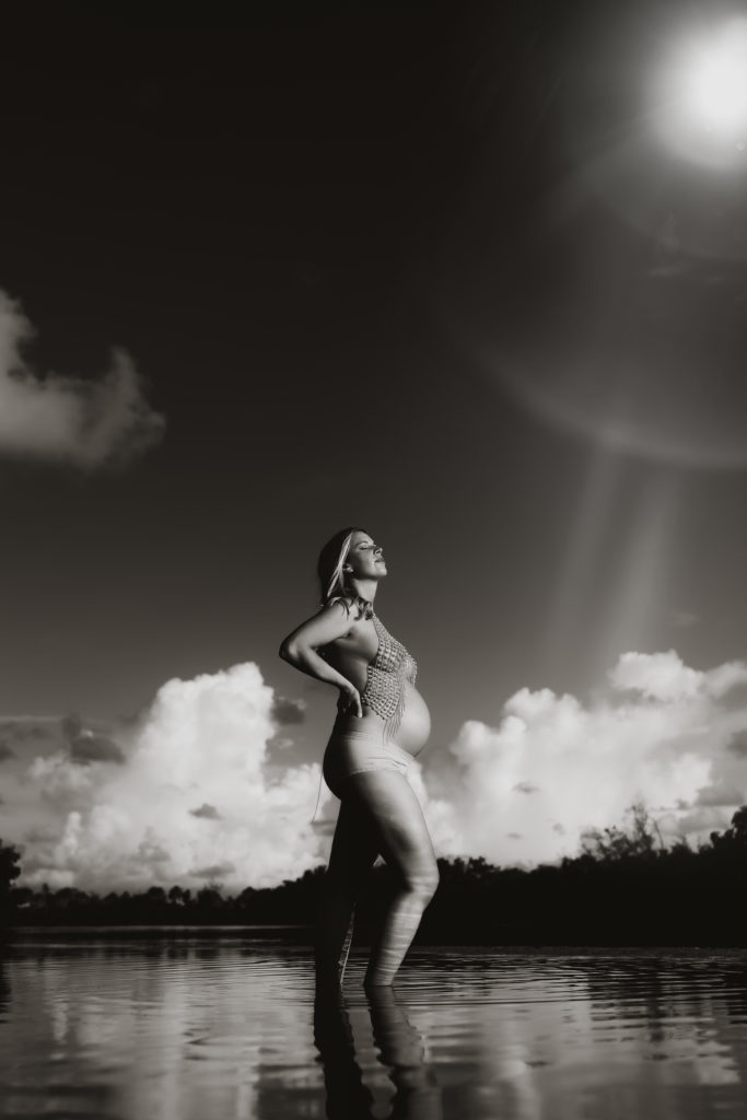 black and white fine art portrait with a pregnant women wearing a gold body chain standing in a pool of water at the beach 
