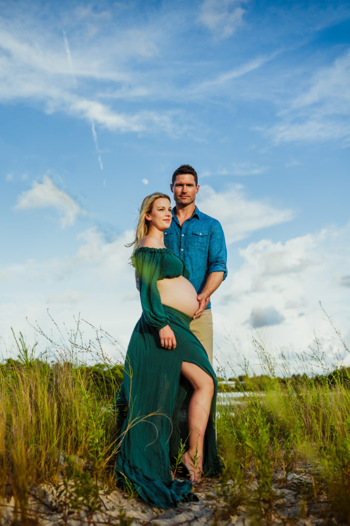 couples beach maternity portrait with a couple in green and blue boho clothing standing in tall grass during a beach pregnancy shoot 