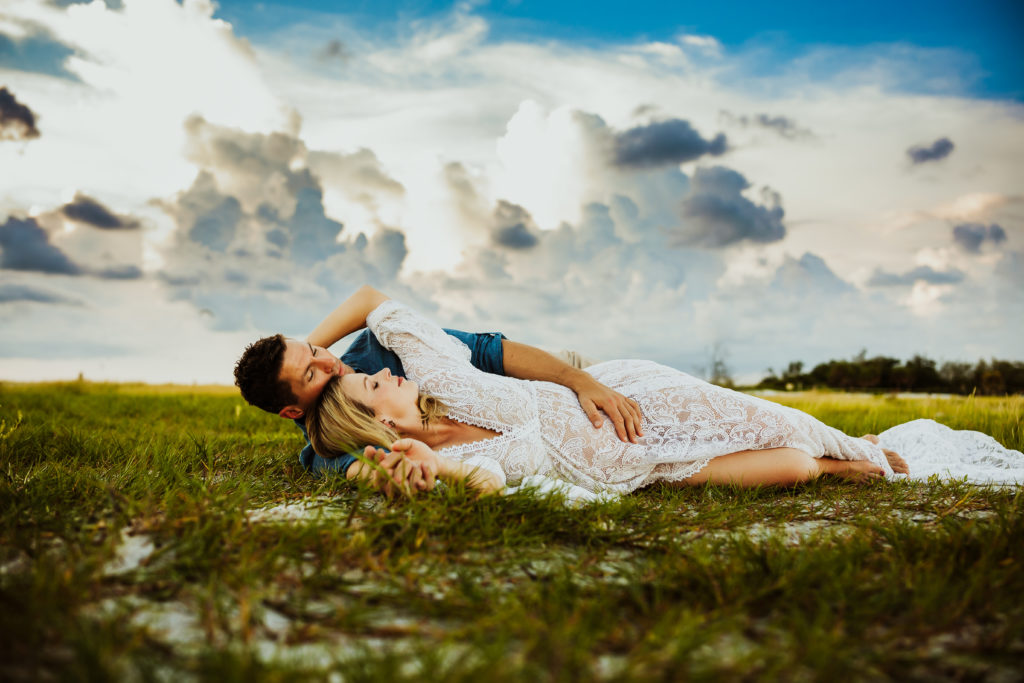 sexy couples pregnancy portrait with a couple laying in the grass on the beach